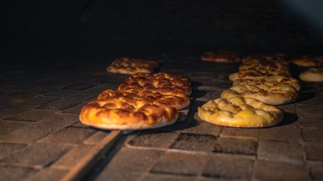 Golden brown bread being baked in a traditional stone oven, showcasing artisanal craftsmanship. - Photo by Yasin Onuş on Pexels