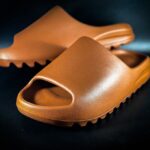 A close-up of brown rubber slides with textured sole on a black background. - Photo by Terrance Barksdale on Pexels