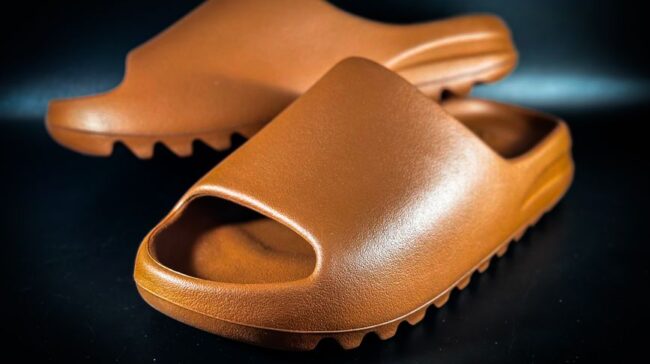 A close-up of brown rubber slides with textured sole on a black background. - Photo by Terrance Barksdale on Pexels