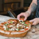 Close-up of a chef slicing a freshly baked artisan pizza in a kitchen setting. - Photo by Anna Shvets on Pexels