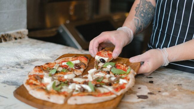 Close-up of a chef slicing a freshly baked artisan pizza in a kitchen setting. - Photo by Anna Shvets on Pexels
